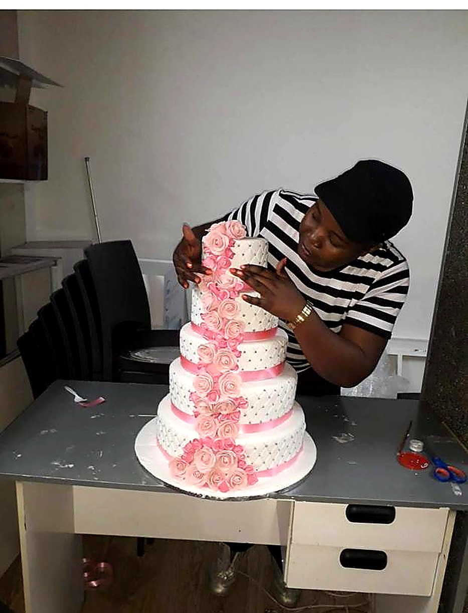 Bakerswell baker arranging pink roses on a four-tier white celebration cake