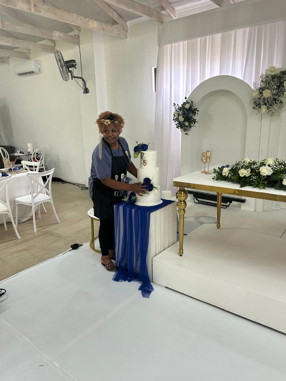 Baker styling a white three-tier wedding cake with blue roses on set
